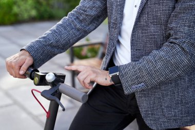 Çevre dostu araç. Elektrikli scooter kullanan, gündüzleri dışarıda duran orta yaşlı şık işadamlarına yakın durun.