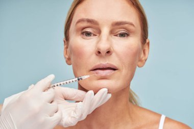 Koruyucu eldivenli doktor dudak büyütme ameliyatı yapıyor.
