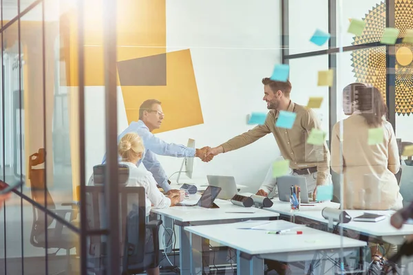 Bonne affaire. Deux hommes d'affaires ou collègues serrant la main lors d'une réunion avec des collègues dans le bureau moderne — Photo