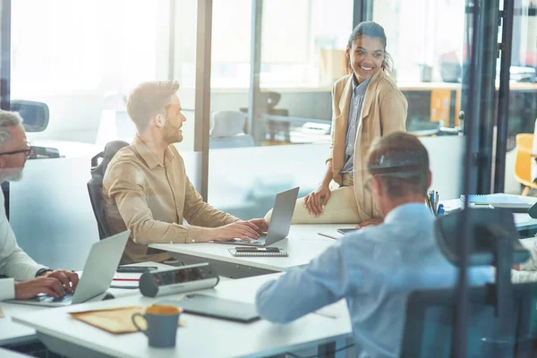 Joven y alegre trabajadora de oficina de raza mixta discutiendo algo con sus colegas mientras está sentada en la sala de juntas en la oficina moderna, gente de negocios teniendo una reunión — Foto de Stock