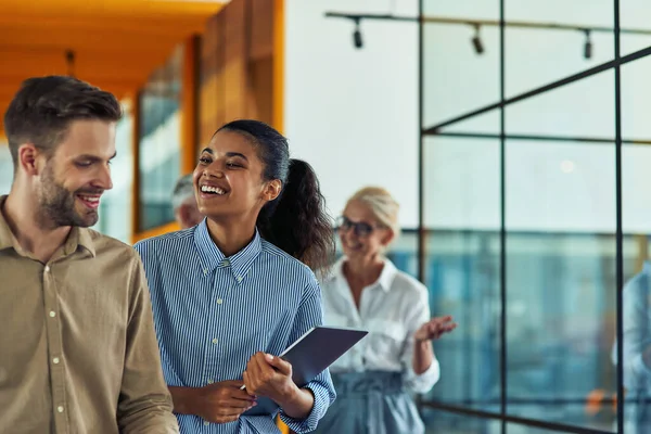 Dos jóvenes colegas alegres y diversos que hablan después de una reunión de negocios mientras están de pie en la oficina moderna o en el espacio de coworking — Foto de Stock