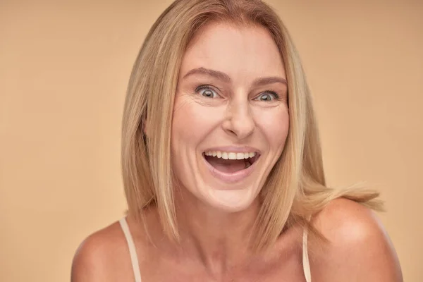 Close up portrait of excited mature woman posing in studio over beige background — Stock Photo, Image