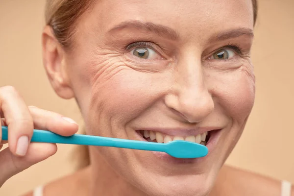 Higiene dental. Sonriente señora madura cuidando de la cavidad oral mientras usa el cepillo de dientes azul — Foto de Stock