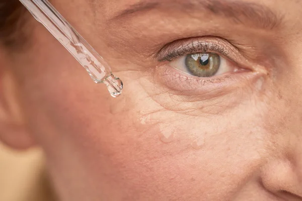 Mujer madura hidratando la piel cerca de los ojos con un suero especial — Foto de Stock