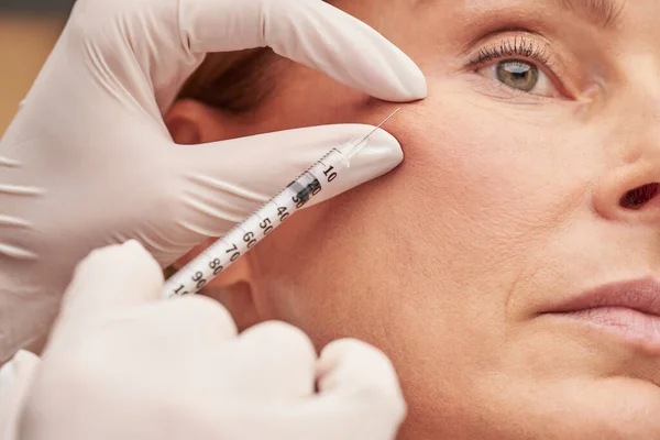 Cosmetología anti envejecimiento. Primer plano de una mujer madura caucásica recibiendo inyección cosmética en su mejilla — Foto de Stock