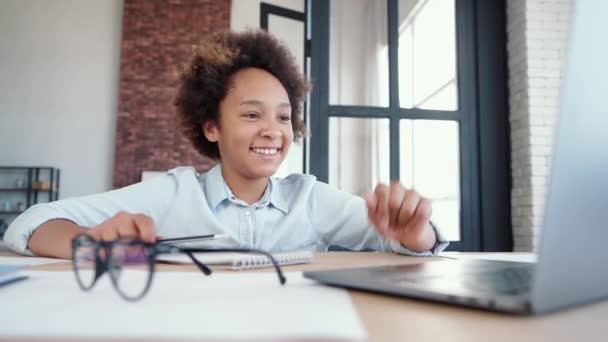 Διασκεδαστική μάθηση. Χαρούμενο έφηβο κορίτσι χαμογελώντας ενώ επικοινωνεί με το δάσκαλό της κατά τη διάρκεια του online μαθήματος και κρατώντας σημειώσεις στο σημειωματάριο, κάθεται στο σπίτι — Αρχείο Βίντεο