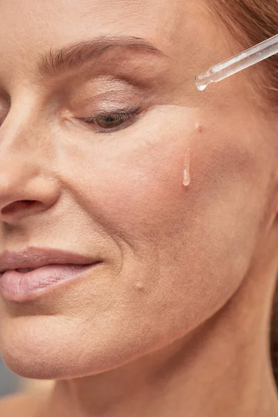 Sonriente dama aplicando aceite esencial en la piel facial y mirando hacia abajo — Foto de Stock