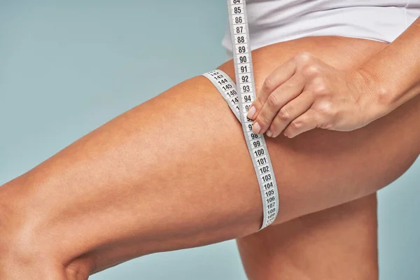 Weight loss. Cropped shot of a woman measuring her leg with a tape measure while standing against blue background
