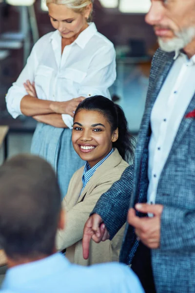 Joven mujer de raza mixta alegre, trabajadora de oficina sonriendo a la cámara mientras tiene una reunión con sus colegas —  Fotos de Stock