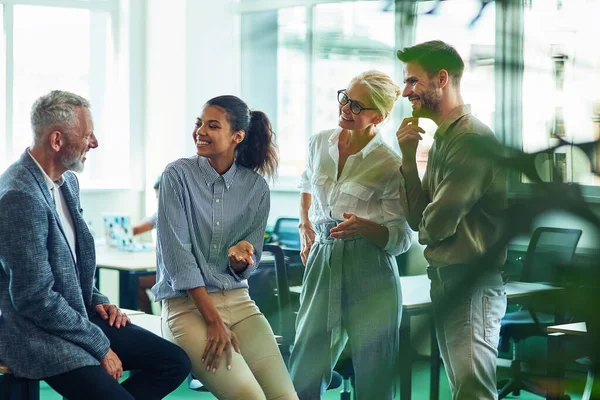 Grupo de gente alegre de negocios que se comunica, discute algo y sonríe mientras está de pie en la oficina moderna o en el espacio de coworking —  Fotos de Stock
