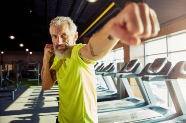 Isınıyorum. Spor giyim boksuna odaklanmış olgun bir adam, spor salonunda çalışırken, erkek yüzüne odaklan.