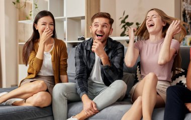 Bulaşıcı kahkaha. Bir grup neşeli, çok kültürlü arkadaş gündelik giysiler içinde modern dairede kanepede otururken birlikte eğleniyorlar.