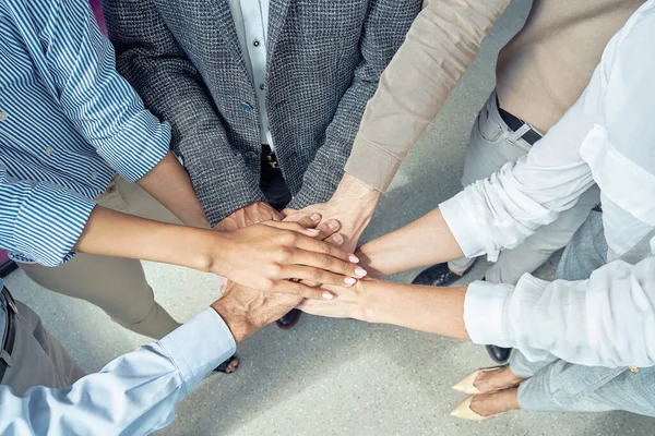 Close up shot of business people putting hands together and smiling, celebrating success while standing at office — Stock Photo, Image