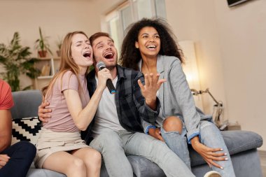Karaokenin tadını çıkar. En iyi arkadaşlar mikrofonla şarkı söylerken mutlu görünüyorlar. Evde karaoke yaparken, modern dairede kanepede otururken.