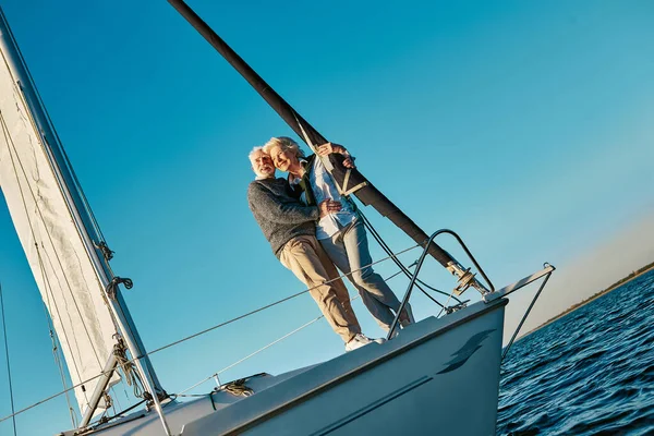 Sakin mavi denizde yüzen yelkenli tekne ya da yat güvertesinde duran romantik ve mutlu yaşlı bir çiftin tam uzunluğu. Sarılmak ve gün batımının tadını çıkarmak. — Stok fotoğraf