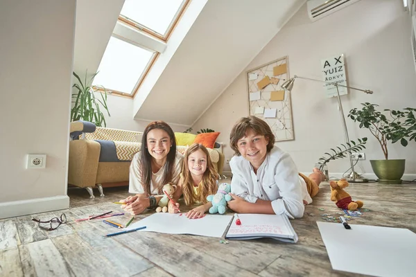 Feliz familia caucásica tendida en el suelo en la sala de estar en casa y sonriendo a la cámara, madre pasando tiempo con los niños — Foto de Stock