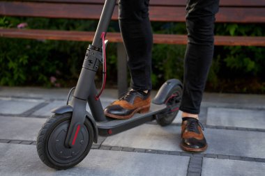 Hızlı ve kullanışlı. Zarif, şık, orta yaşlı iş adamının dışarıda elektrikli scooterıyla dikilirken yakın plan çekimi.