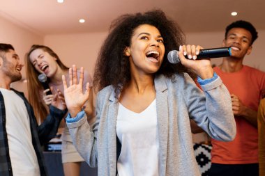 Şarkı söylemeye devam. Mikrofon tutan ve en iyi arkadaşlarıyla karaoke partisinde şarkı söyleyen oldukça karışık ırk kızı mutlu görünüyor. Mutlu çok kültürlü insanlar birlikte vakit geçiriyor.