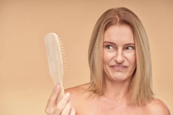 Problema de pérdida de cabello. Frustrado y molesto mujer rubia madura mirando peine — Foto de Stock