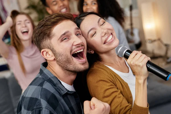 Hidupkan lagu itu. Pasangan muda yang bersemangat atau teman-teman memegang mikrofon dan bernyanyi bersama sambil bermain karaoke dengan teman-teman di rumah. Kelompok orang bersenang-senang di karaoke rumah pesta — Stok Foto
