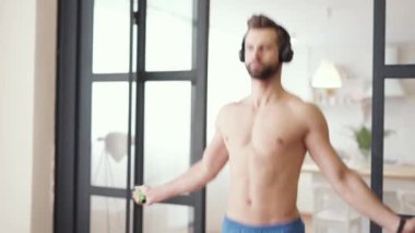 Kardiyo çalışması. Çıplak gövdeli, kulaklık takan yakışıklı, beyaz tenli bir sporcu. Evde ip atlamakla uğraşırken odaklanmış görünüyor.
