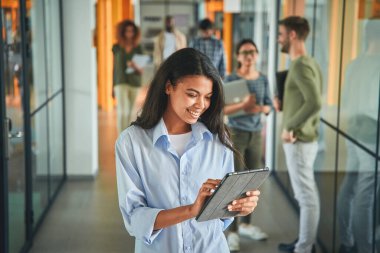 Meslektaşları sohbet ederken tablet kullanan neşeli genç bir kadın.
