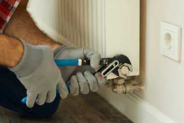 Isıtma sistemi. Erkek ellerinin ayarlanabilir ingiliz anahtarıyla yakın çekimi. Tamirci ısıtma kaloriferini tamir ediyor.