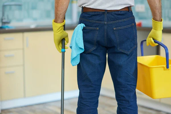 Temizlik gurusu. Profesyonel erkek temizlikçi eldiven giyer, plastik kova ve paspas taşır ve mutfakta yerleri temizlemeye hazırlanır. — Stok fotoğraf