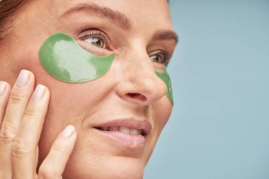 Mavi arka planda dikilirken göz bandı kullanan güzel bir kadının portresini kapat.