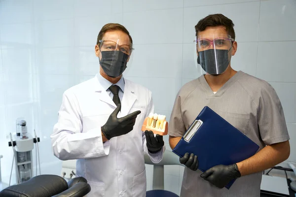 Dentistas en equipos de protección personal posando en el lugar de trabajo — Foto de Stock
