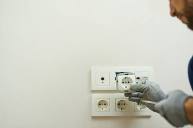 Elektrikçinin koruyucu eldiven giyip eve yeni soket takarken yakın plan çekimleri.