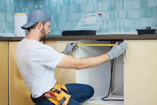 Mladý opravář, profesionální instalatér pomocí měřicí pásky při provádění instalatérských prací v novém bytě po opravě — Stock fotografie