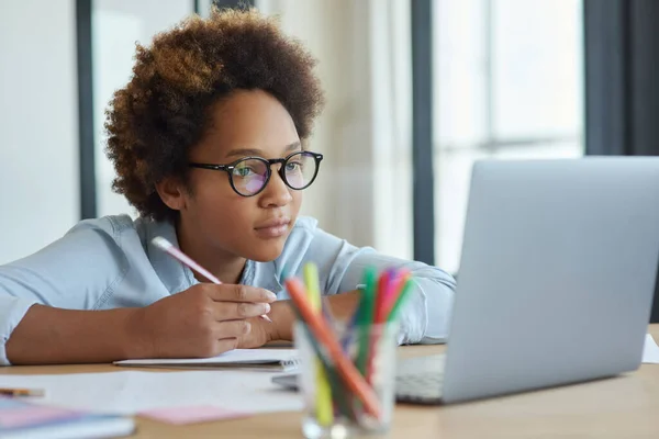Antusiasme ras gadis remaja ras campuran berkacamata mendengarkan gurunya, membuat catatan, menggunakan laptop selama pelajaran video online saat belajar dari rumah — Stok Foto