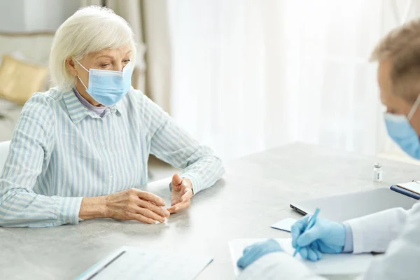 Mujer mayor en máscara médica hablando con el médico en la clínica — Foto de Stock