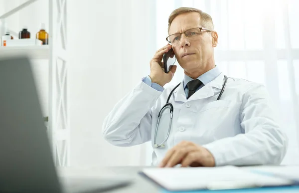 Bonito médico masculino tendo conversa telefônica na clínica — Fotografia de Stock