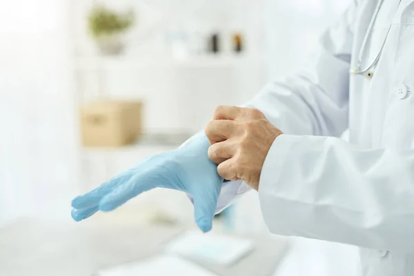 Männlicher Arzt zieht in Klinik sterile blaue Handschuhe an — Stockfoto