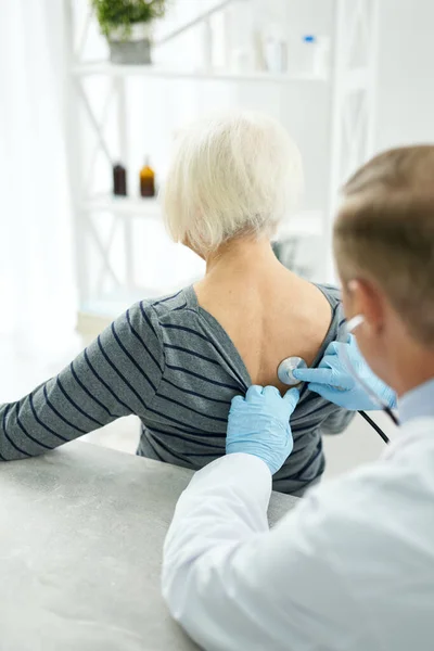 Médico en guantes estériles examinando a una anciana con estetoscopio — Foto de Stock