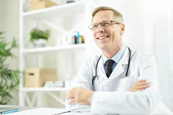 Alegre médico masculino sentado a la mesa en el trabajo — Foto de Stock