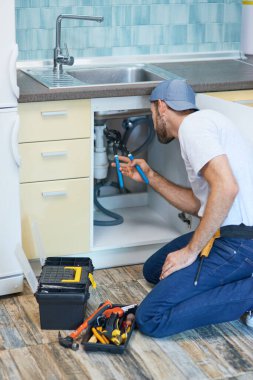 Tesisat sorunları. Profesyonel tesisatçı mutfaktaki lavabo borusunu tamir ederken boru anahtarı kullanıyor.