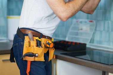 Güvenilir onarımlar. Kapalı alanda mutfak sökücü tamir eden kemer takan genç bir işçinin kırpılmış görüntüsü.