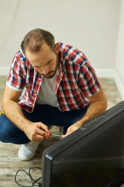 Reliable home repair. Serious repairman looking focused, holding a screwdriver while installing or fixing tv set in apartment of a customer