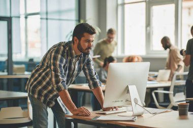 Ofis bilgisayarında çalışan esmer adam.