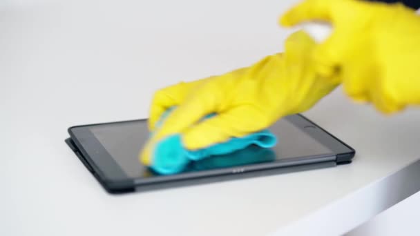 Disinfect your gadgets. Close up of female hands in protective yellow gloves cleaning screen of tablet pc with alcohol spray on a white background — Stock Video