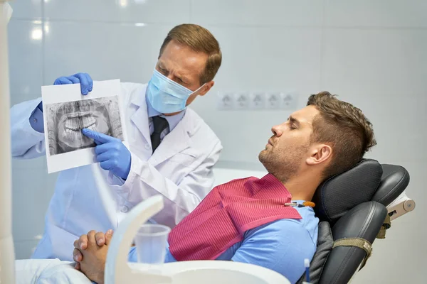 Worried dental surgeon holding an x-ray image near his patient — Stock Photo, Image