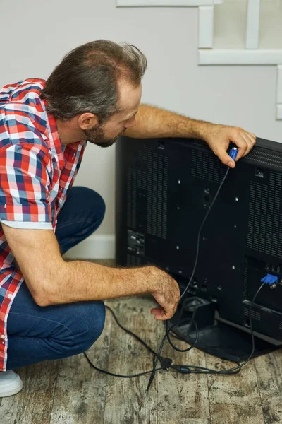 Installation process. Handyman looking focused, holding tv cable while installing or fixing tv set in apartment of a customer