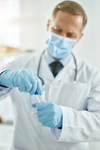 Healthcare worker in medical mask holding test tube