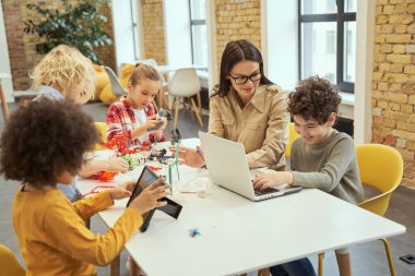 Proje. Gözlüklü genç bayan öğretmen, sınıfta dizüstü bilgisayar kullanarak küçük bir çocuğa bilimsel robot videosu gösteriyor.