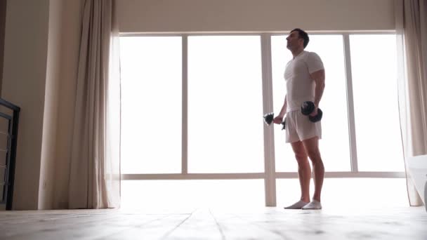Keep training. Full length view of active caucasian man wearing home clothes exercising with dumbbells at home — Vídeo de Stock