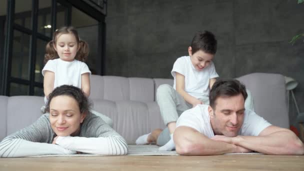 Розслабся. Красива дочка і син роблять масаж для своїх батьків, посміхаючись, сидячи на батьків, проводячи час разом вдома — стокове відео