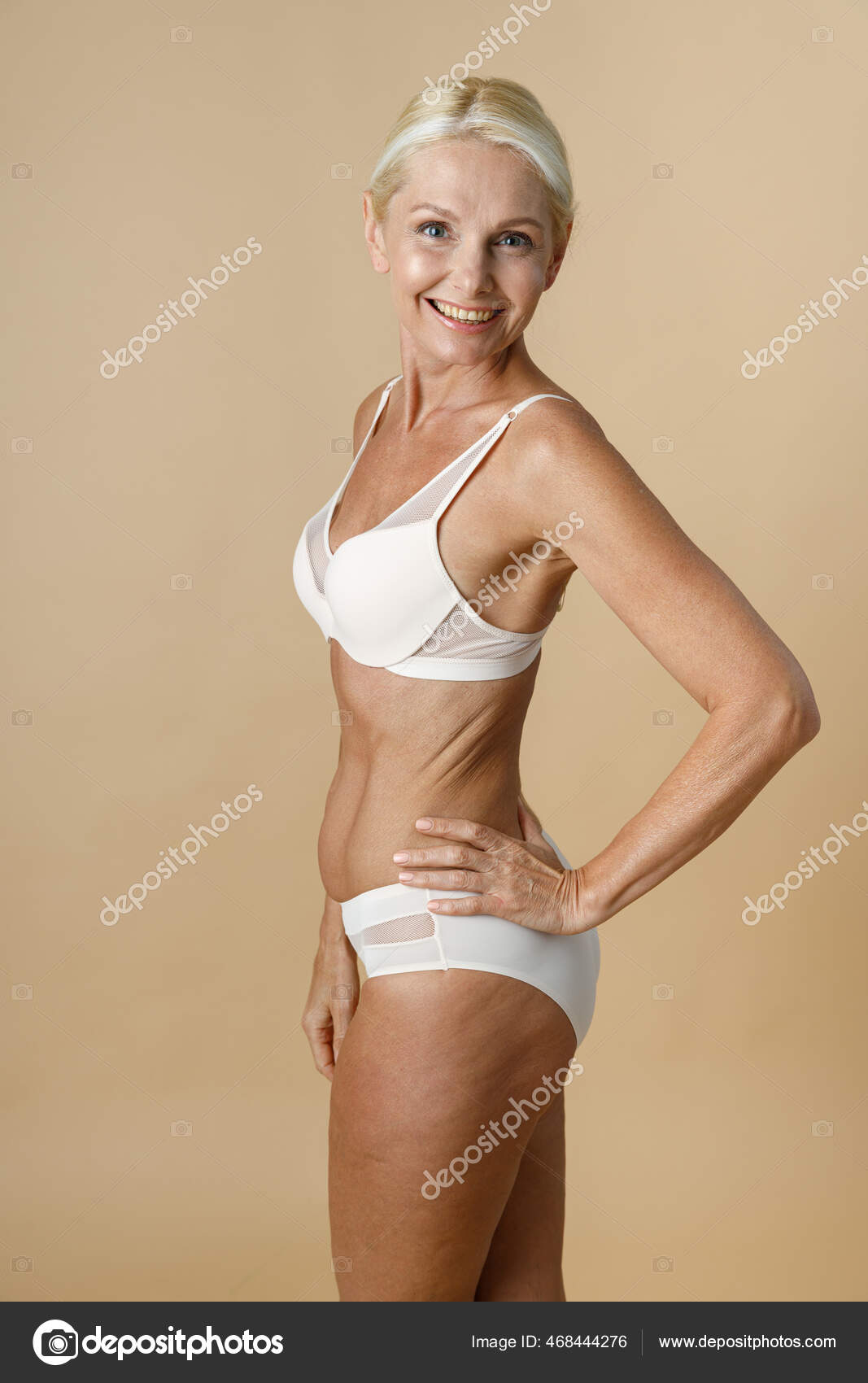 Pretty mature woman in underwear with fit body turning head to camera and  smiling, holding hand on waist standing isolated over beige background  Stock Photo by ©kostiantynvoitenko 468444276